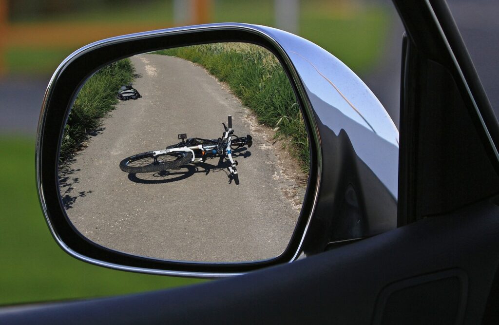 Road traffic accident liability shown through a car mirror reflecting a fallen bicycle after a collision.