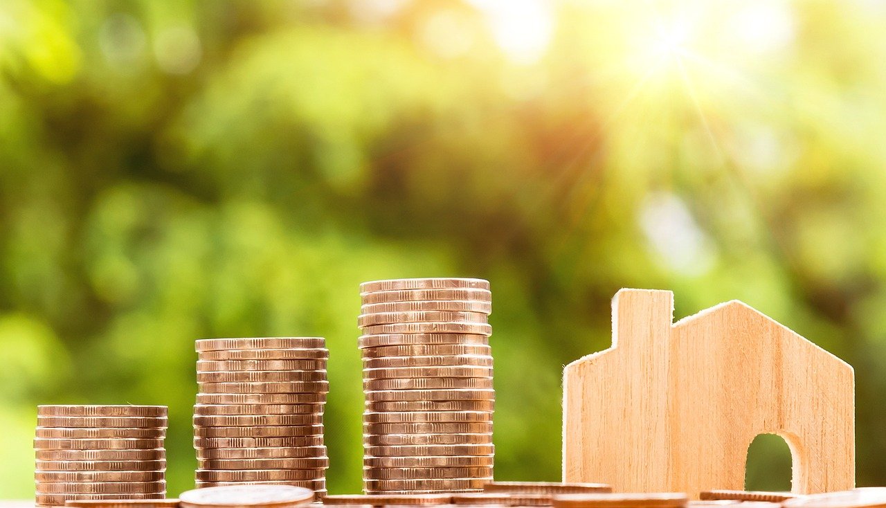 Stacks of coins next to a small wooden house model representing property investment opportunities amid falling Mortgage Rates UK.