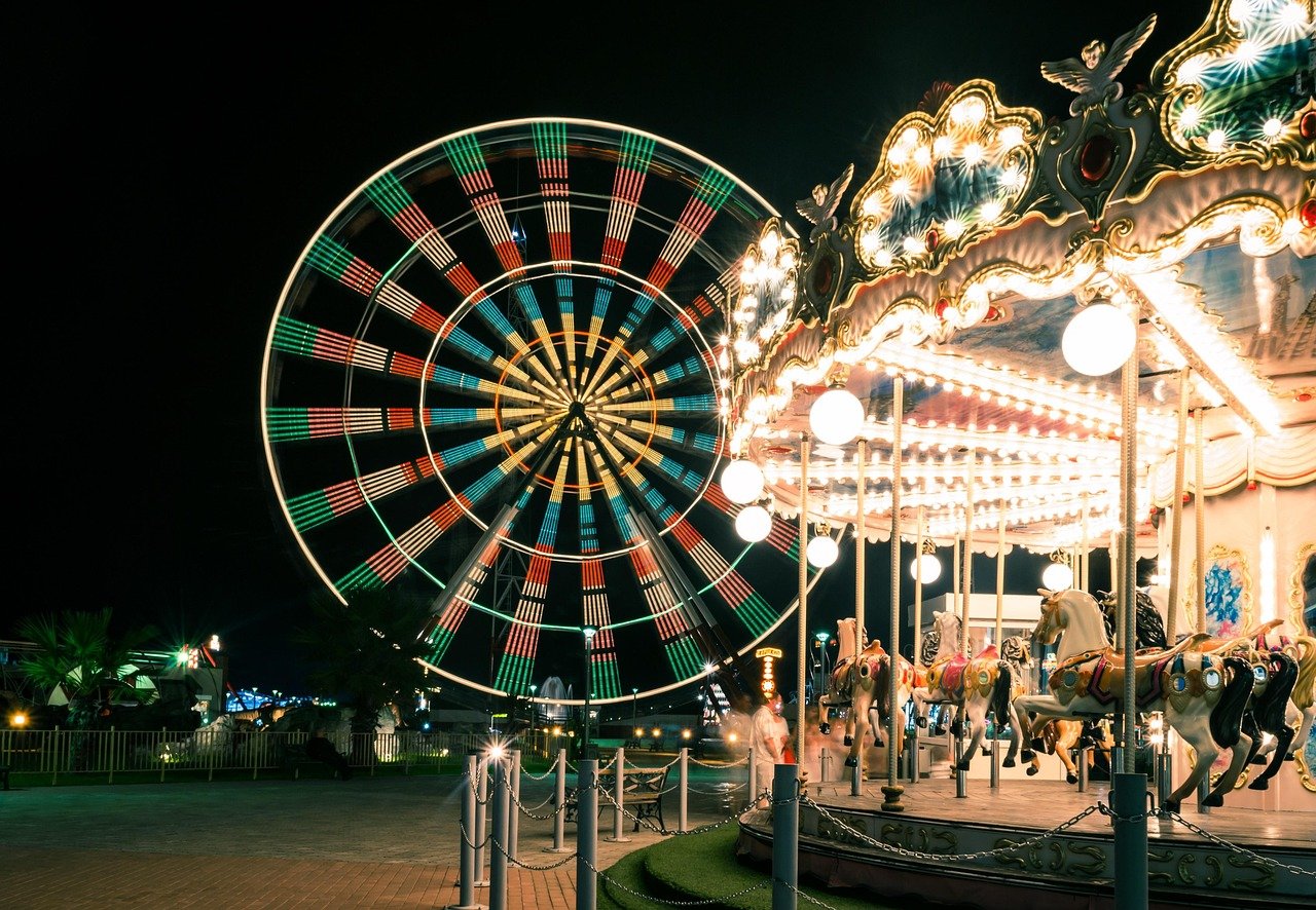 Colourful Ferris wheel and illuminated carousel at night in a carnival setting.